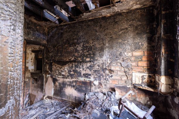 A burnt-out room featuring a broken window and door, illustrating the aftermath of fire damage restoration efforts.